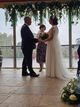 Sylvie officiates the wedding ceremony as the bride and groom hold hands under a floral display.