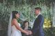 Sylvie officiating the ceremony while the bride and groom hold hands and look at each other.