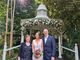 Sylvie standing with the bride and groom in front of a gazebo and trees.